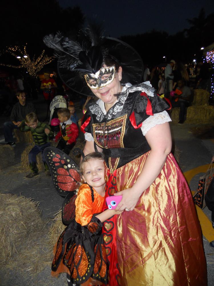Woman dressed in intricate dress and mask hugs young girl in monarch butterfly dress